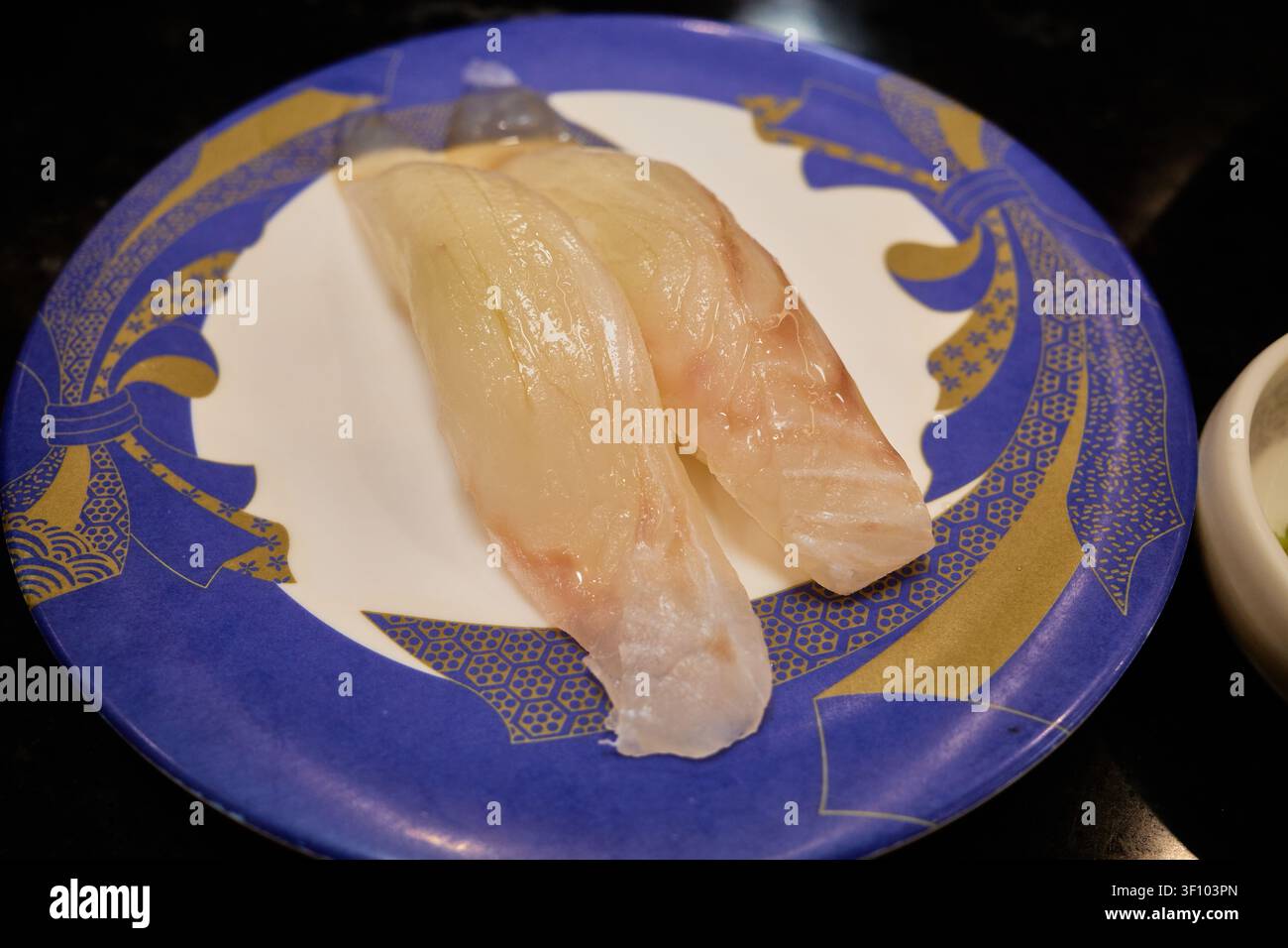 Verschiedene Premium-Nigiri-Sushi-Sorten, darunter frischer Weißfisch und gebratener Fisch mit Kreuzhatch-Schnitt, serviert auf bunten Tellern an einem modernen Transportband Stockfoto