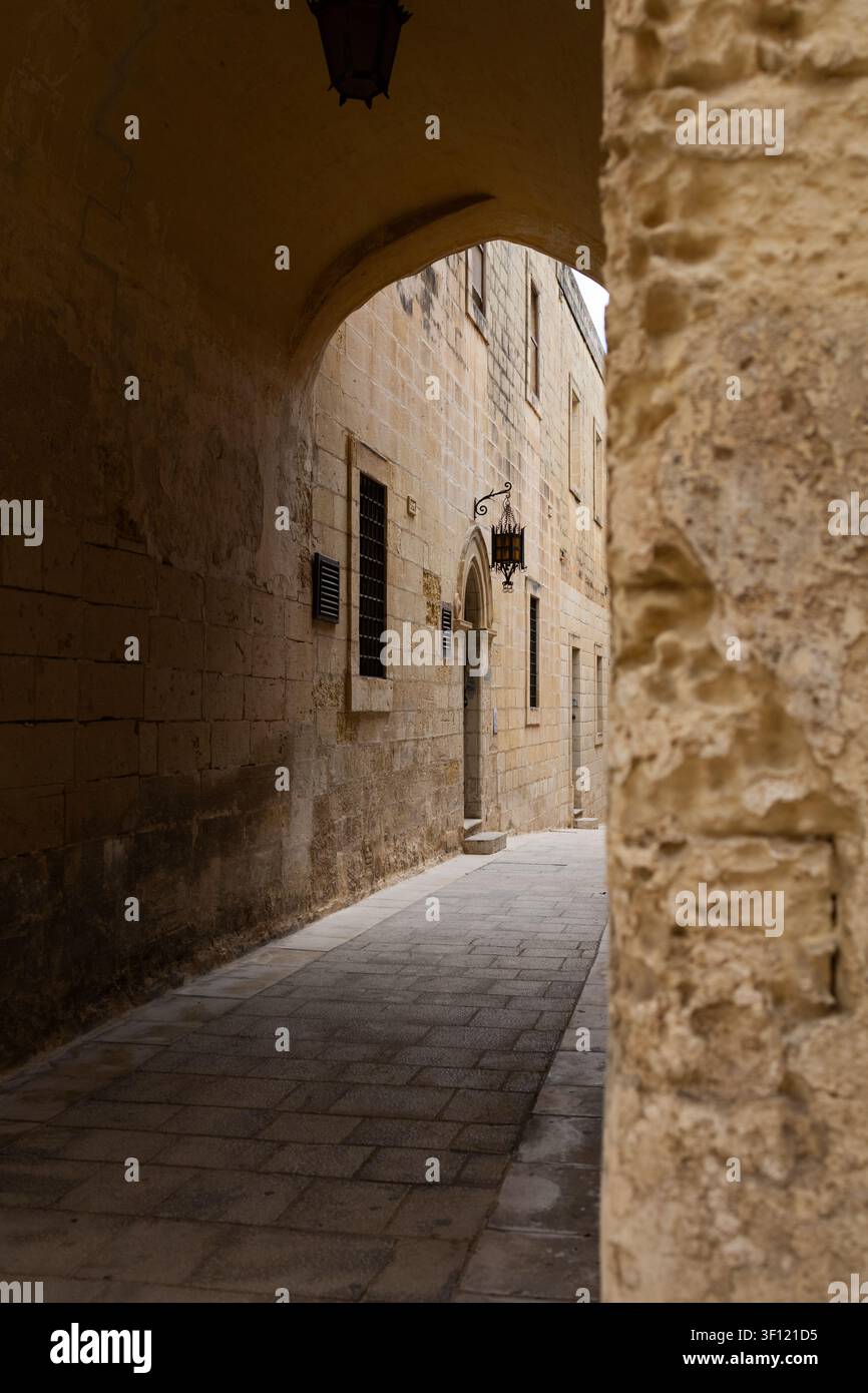 Ansicht einer historischen mittelalterlichen Steinstraße, eingerahmt von einem antiken Torbogen in Malta. Stockfoto