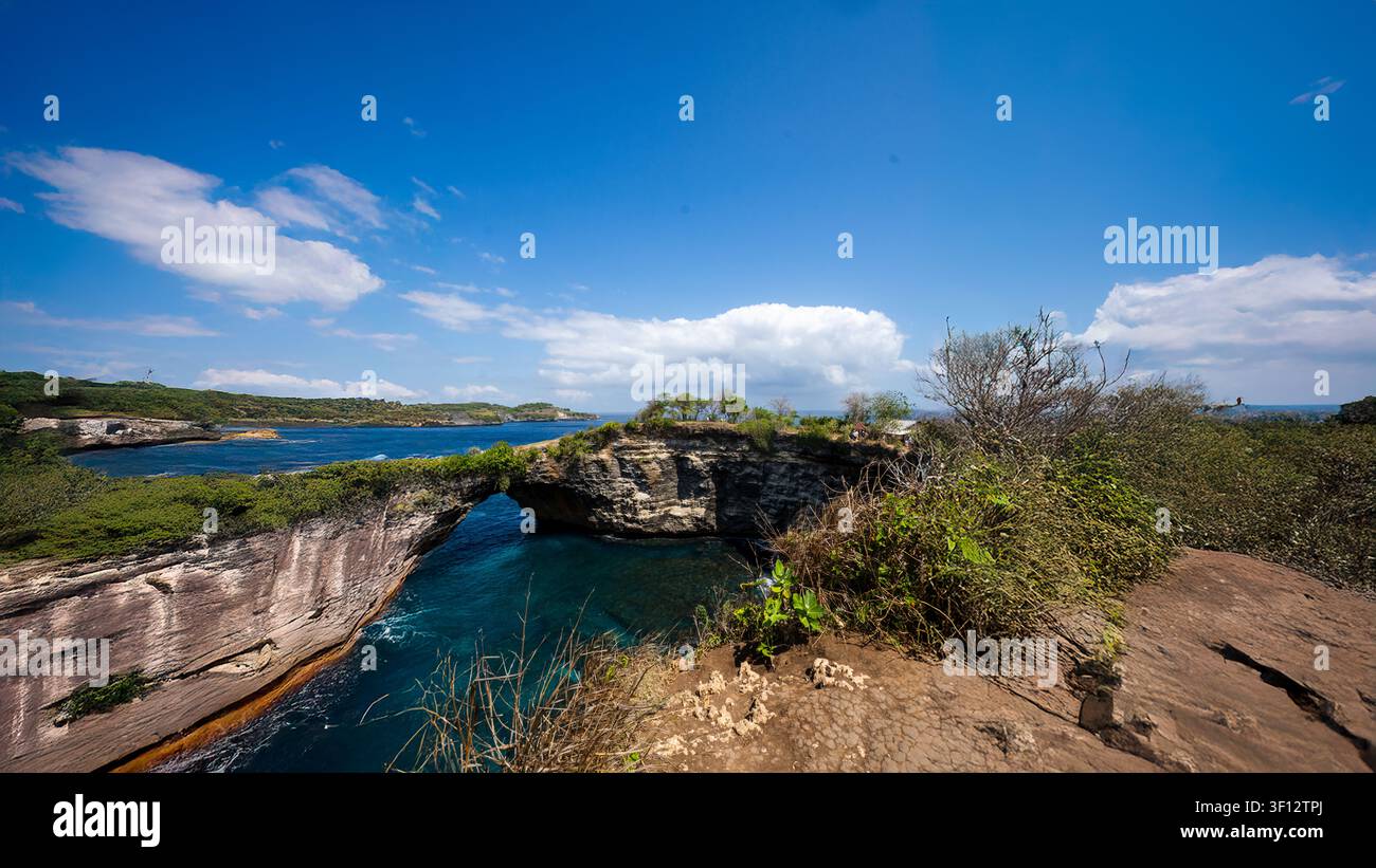 Dramatischer natürlicher Kalksteinbogen mit Blick auf tiefblauem Ozean, eingerahmt von Küstenvegetation und sonnigem Himmel. Stockfoto