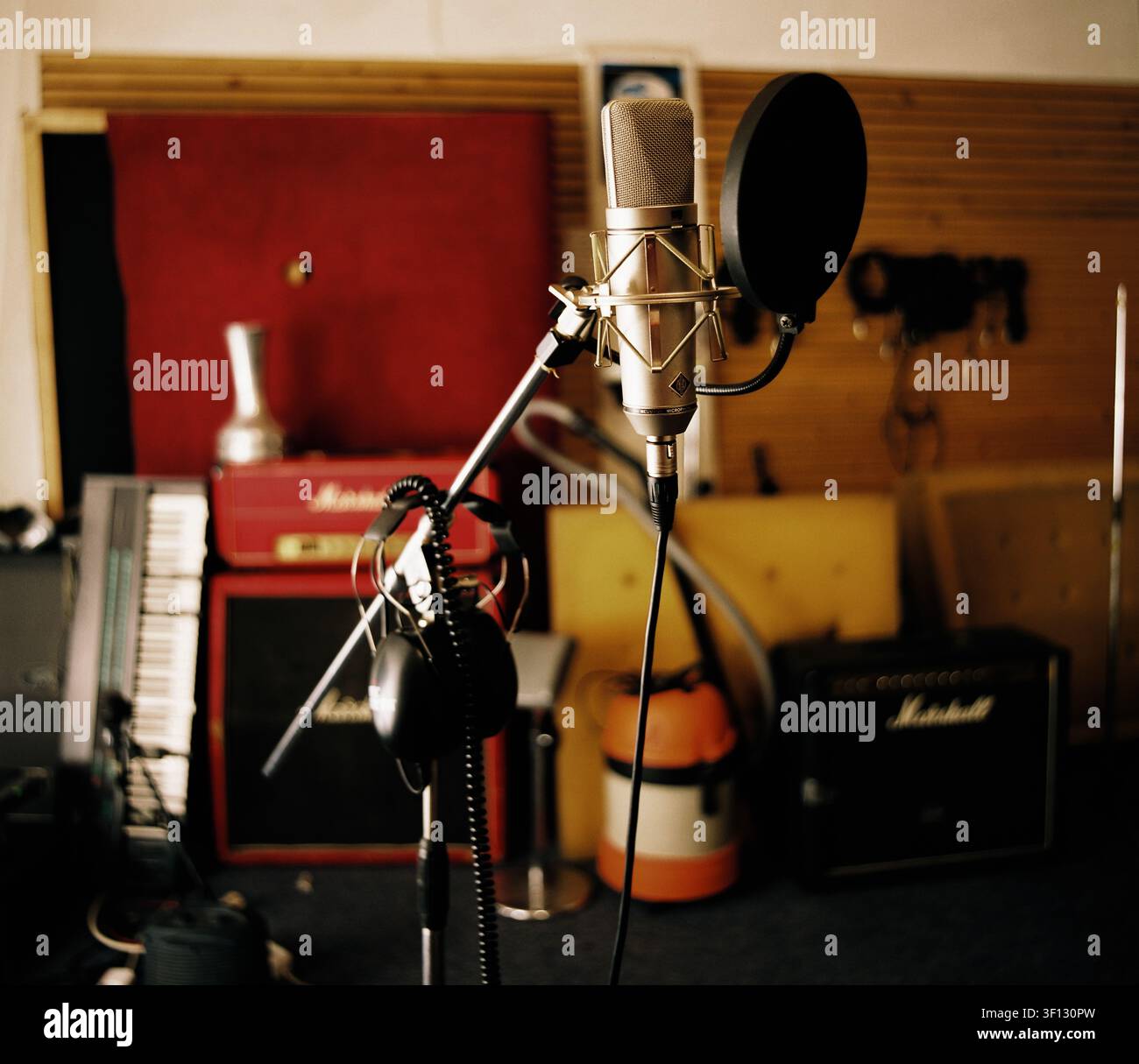 Studiumikrofon mit Popfilter bereit für Gesangsaufnahme, mit Verstärkern und Tastaturen weich im Hintergrund unscharf, aufgenommen mit Pentacon Six. Stockfoto