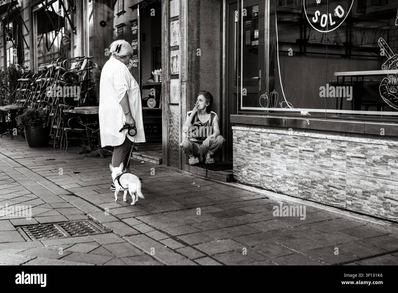 Frau mit einem kleinen Hund spricht mit einer sitzenden Frau vor einem Restaurant in der Altstadt von Bratislava, Slowakei. Stockfoto