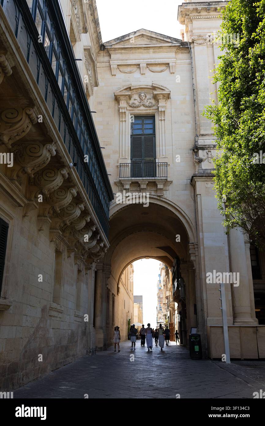 Grander historischer Steinbogen mit traditionellen Holzbalustern und gehenden Menschen in Malta. Stockfoto