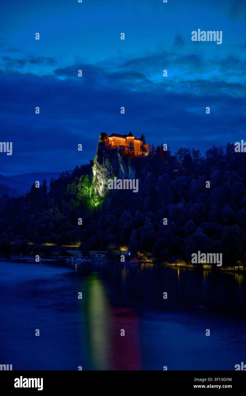 Illuminierte Burg Bled und die Pfarrkirche St. Martin, die sich in der blauen Stunde auf dem Bledsee in Bled, Slowenien, spiegeln. Stockfoto