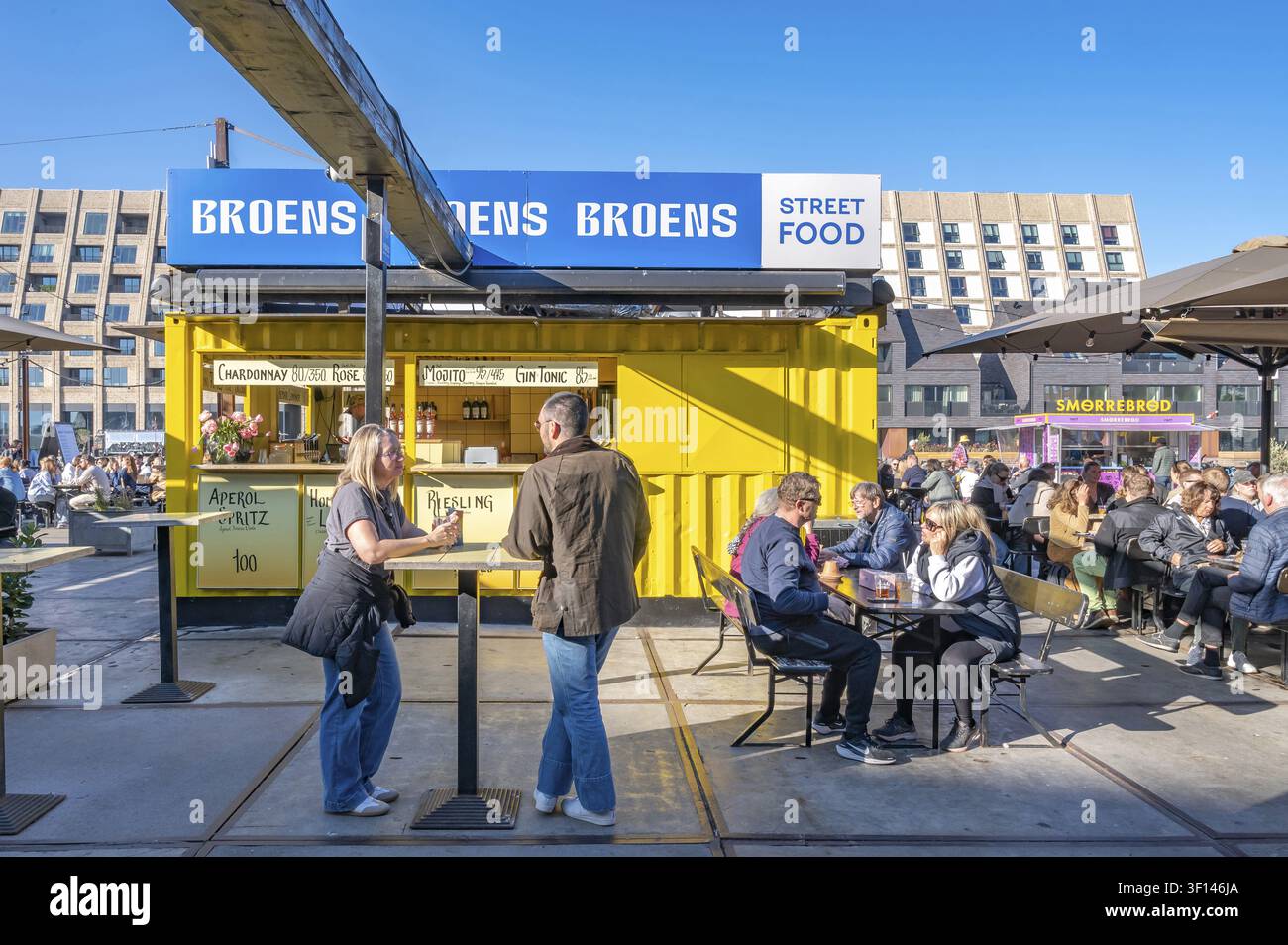 Ein Blick auf einen gelben Getränkekiosk am Broens Gadekokken (Broens Street Food) Straßenfood-Markt, vor dem Gäste an Bartischen sitzen a Stockfoto