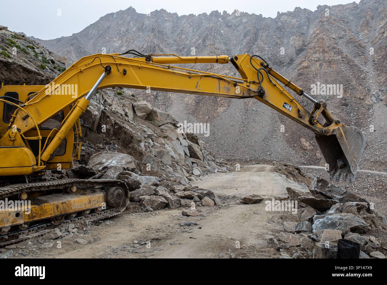 Ein großer gelber Kettenbagger arbeitet daran, Felsbrocken und Schutt von einer Schotterbergstraße in Ladakh, Indien, zu entfernen und einen von einer Lanze versperrten Weg freizuräumen Stockfoto
