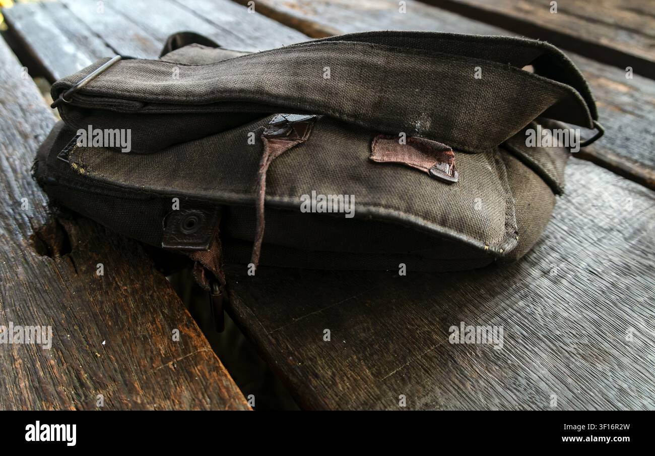 Abgenutzte Schultertasche aus Canvas, die auf einem rustikalen Holztisch ruht, repräsentiert alltägliches Tragen, Reisen, Einfachheit und langlebigen täglichen Gebrauch. Stockfoto
