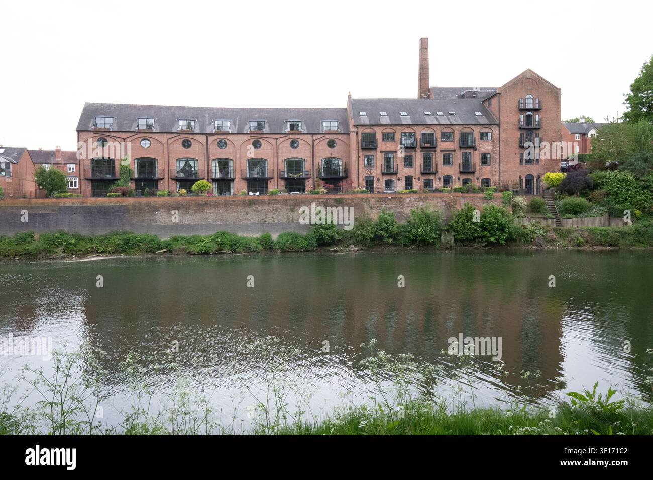 Umgebaute Backsteinmühlenwohnungen spiegeln sich im ruhigen Wasser des Flusses Severn in Shrewsbury, Shropshire, an einem bewölkten Tag wider. Stockfoto