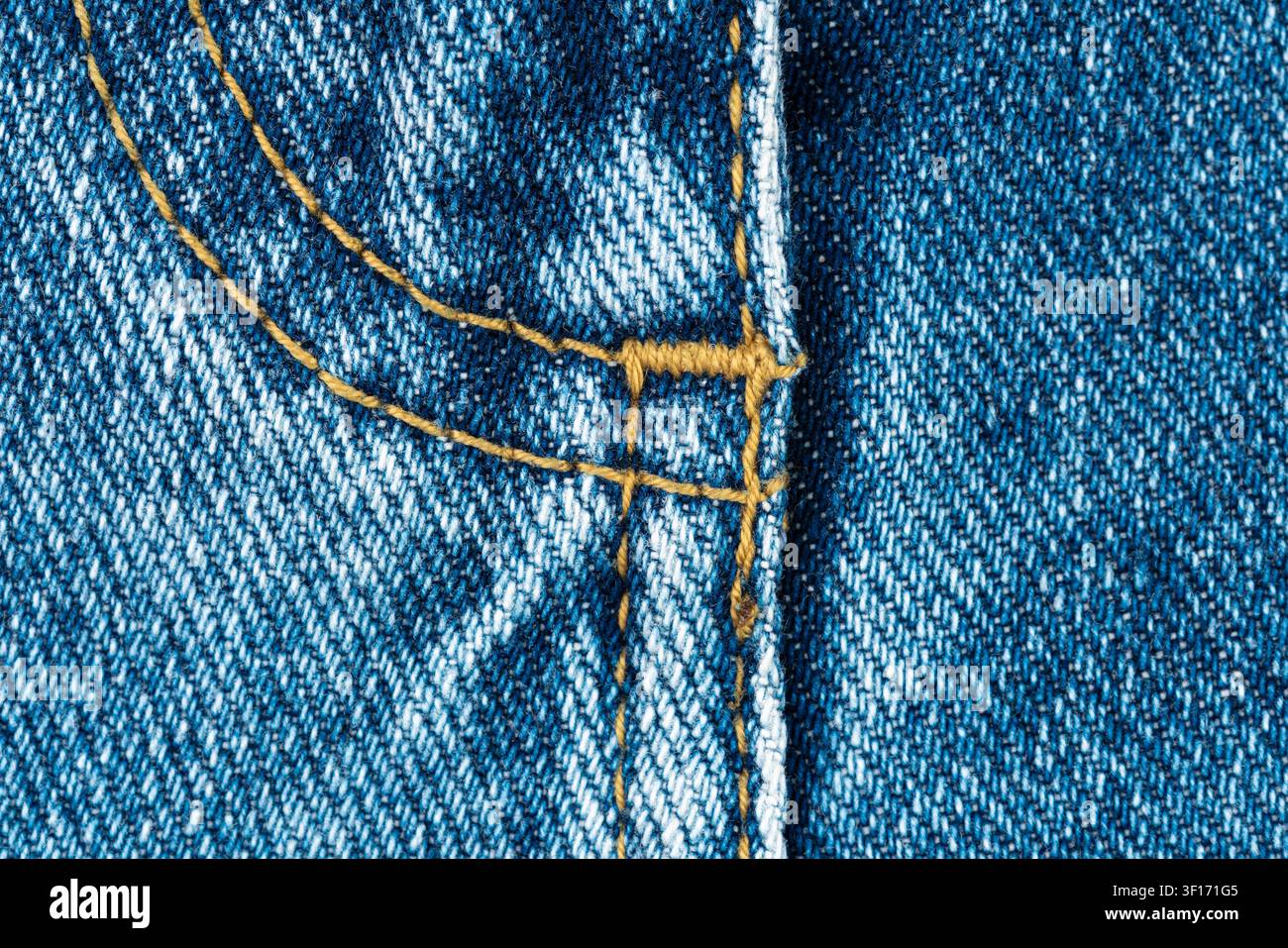 Strukturierter blauer Denim im Nahaufnahme mit kontrastierender gelber Naht, die ein geometrisches Muster bildet, Reißverschluss im Schritt. Hervorgehobener Webnaht-Detail bei gleichmäßiger Beleuchtung. Id Stockfoto