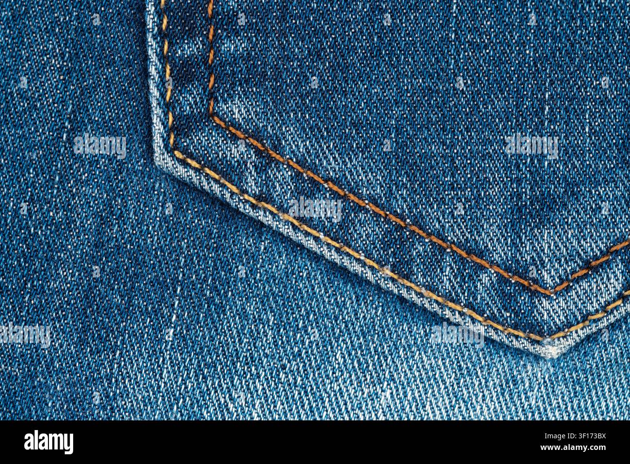Strukturierter blauer Denim im Nahaufnahme mit diagonaler Taschennahnaht und kontrastierender orangefarbener Stickerei. Gewebtes Baumwollstoffgefüge sichtbar bei gleichmäßiger Beleuchtung. Ide Stockfoto