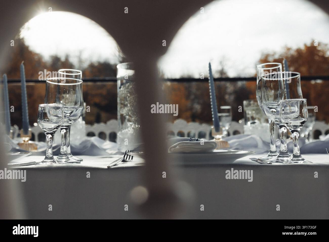 Leerer Tisch für ein elegantes Abendessen gedeckt. Gläser, Teller und Besteck ordentlich angeordnet. Weiches Tageslicht fällt durch den gewölbten Fensterrahmen. Hinweis auf Außenansicht Stockfoto