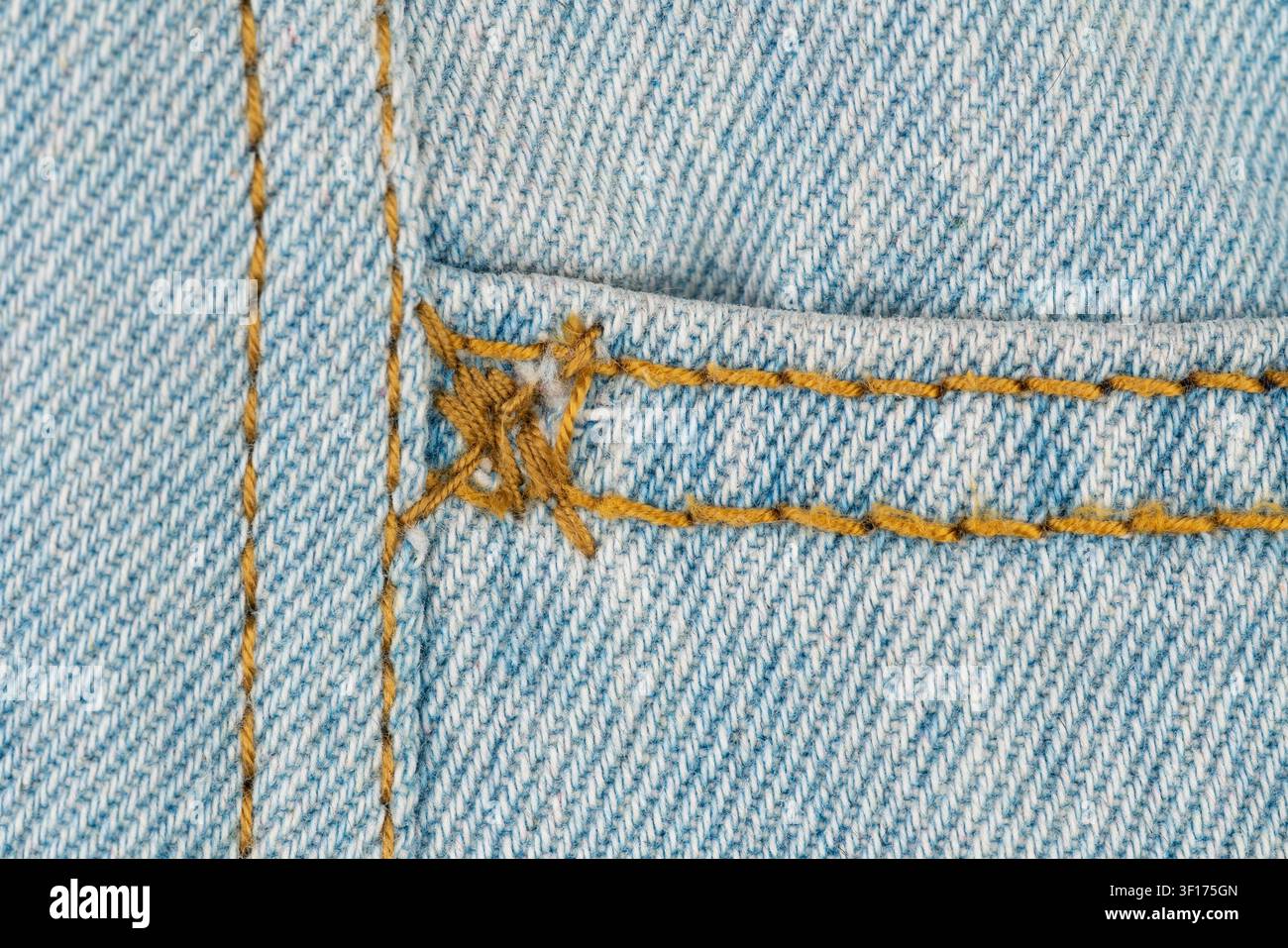 Makroaufnahme von hellblauer Denimtextur mit deutlicher gelber Naht. Abgenutzte Taschenecke zeigt ausgefranste Fäden und Stoffverlauf. Gewebemuster Textil Stockfoto