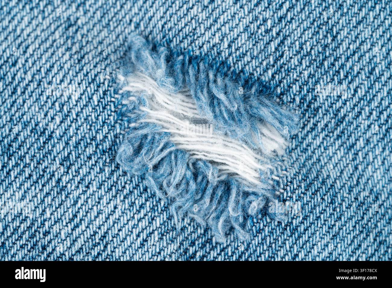 Detaillierte Makroaufnahme von abgenutztem blauem Denim mit sichtbarer Gewebestruktur, ausgefranster Rippe, die weiße Innengarnfäden freilegt. Weiches natürliches Licht hebt den Stoff hervor Stockfoto