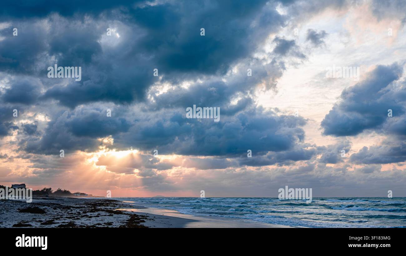 Wunderschöner Sonnenuntergang über dem Strand mit dramatischen Wolken und schimmernden Meereswellen. Stockfoto