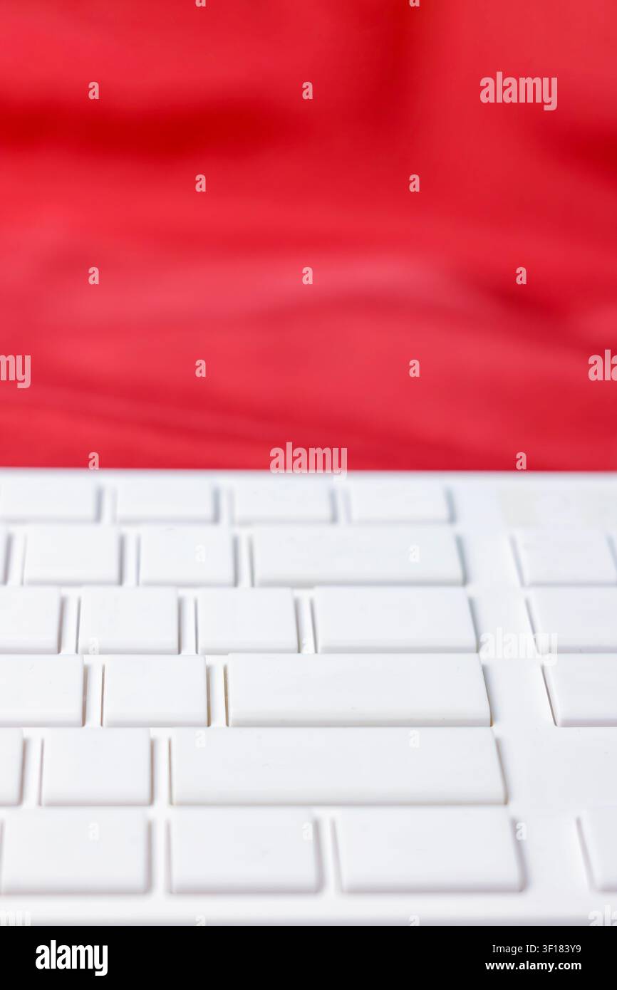 Eine vertikale Makrofotografie konzentriert sich auf die sauberen, leeren Tasten einer modernen weißen Computertastatur, wobei eine weiche, unscharfe rote Stoffoberfläche die obere Hälfte des Bildes ausfüllt. Das minimalistische Bild repräsentiert Technologie, Dateneingabe, digitale Kommunikation, Texten und Online-Sicherheit. Hochwertiges Foto Stockfoto