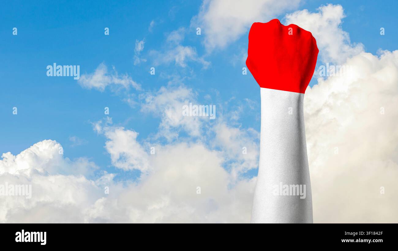 Eine konzeptionelle Nahaufnahme eines menschlichen Arms und einer geballten Faust, die in den roten und weißen Farben der indonesischen Flagge gemalt ist und hoch gegen einen lebendigen blauen Himmel mit flauschigen weißen Wolken erhoben wird. Hochwertiges Foto Stockfoto