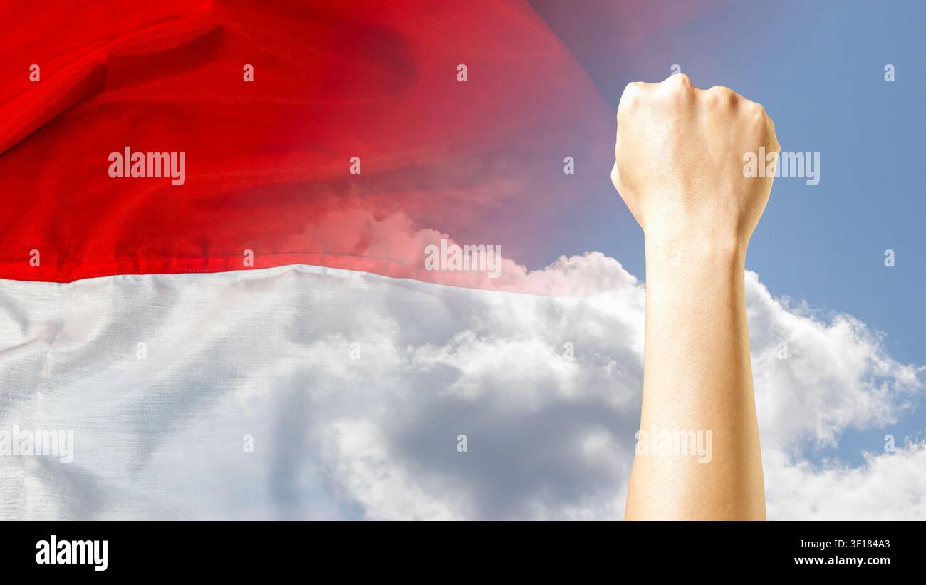 Eine kraftvolle menschliche geballte Faust, die hoch in der Luft gegen einen Doppelbelichtungs-Hintergrund aus der wehenden indonesischen Flagge und einem klaren blauen Himmel mit weißen Wolken erhoben wird. Hochwertiges Foto Stockfoto