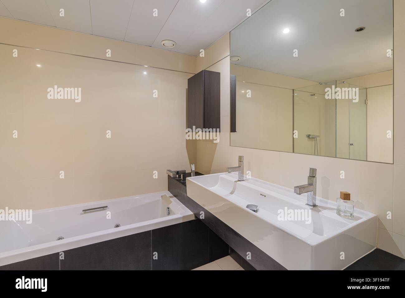 Zeitgenössisches Badezimmerinterieur mit weißer eingebauter Badewanne, Doppelbewaschtisch, großem Wandspiegel, Chrom-Armaturen, hellen neutralen Oberflächen, geräumig Stockfoto