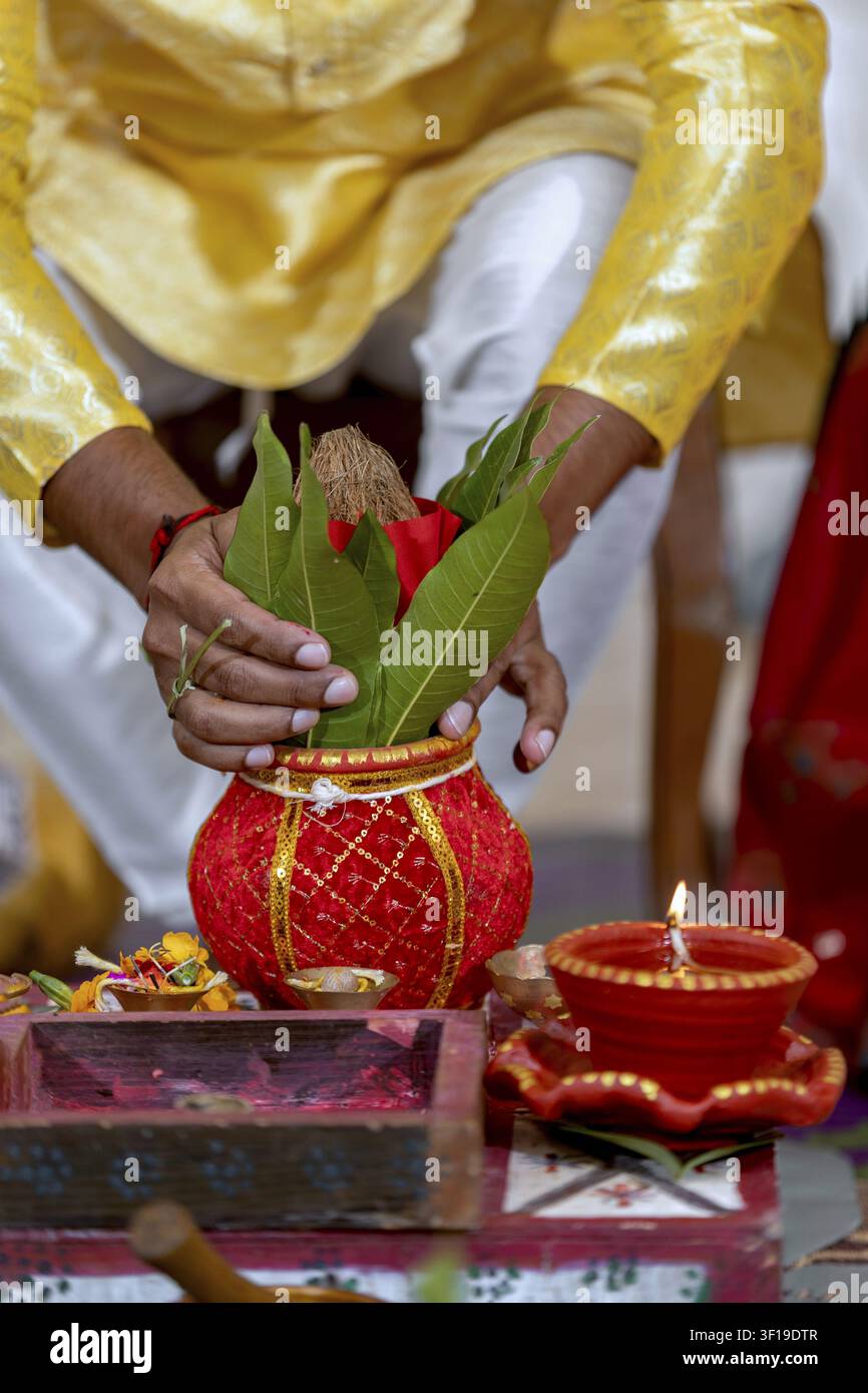 Eine Person in traditioneller indischer Kleidung führt eine religiöse Zeremonie durch und hält einen verzierten Kalash-Topf, der mit heiligen Gegenständen gefüllt ist, und einen brennenden Diya Stockfoto