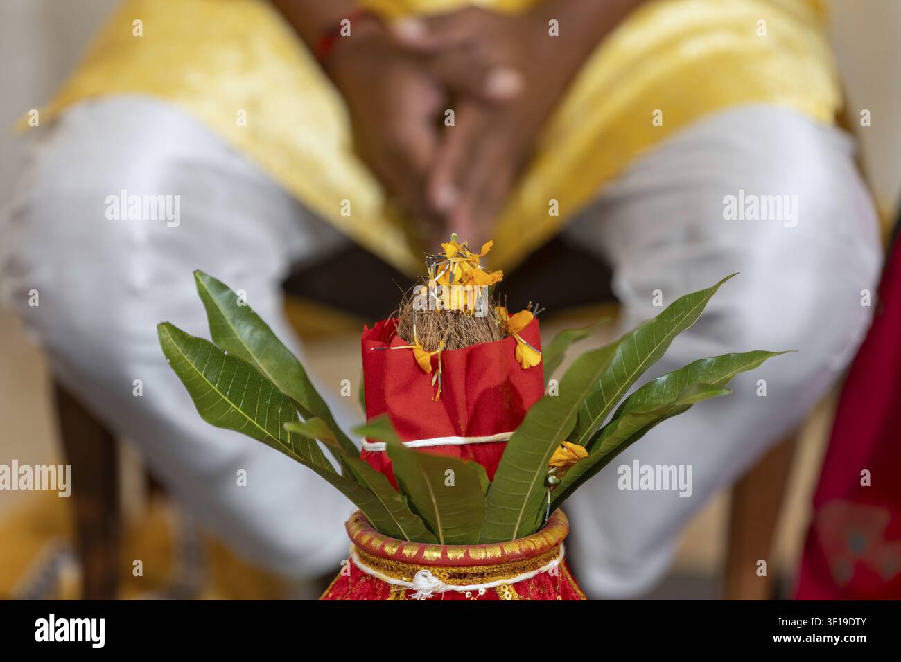 Ein heiliger Kalash, geschmückt mit Mangoblättern und Blumen, wird vor einer betenden Person während eines traditionellen indischen Rituals gehalten Stockfoto