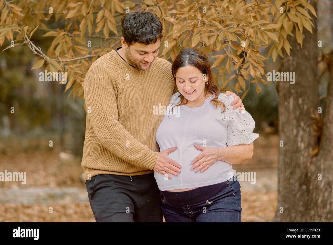 Schwangeres Paar hält einen schwangeren Bauch in einer warmen herbstlichen Außenszene, drückt Liebe, Vorfreude, familiäre Verbundenheit und emotionale Momente aus Stockfoto
