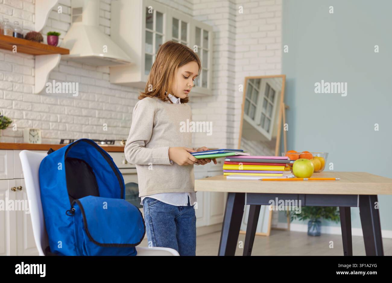 Kind bereitet farbenfrohe Schulbücher neben einem blauen Rucksack auf einem Holztisch vor Stockfoto