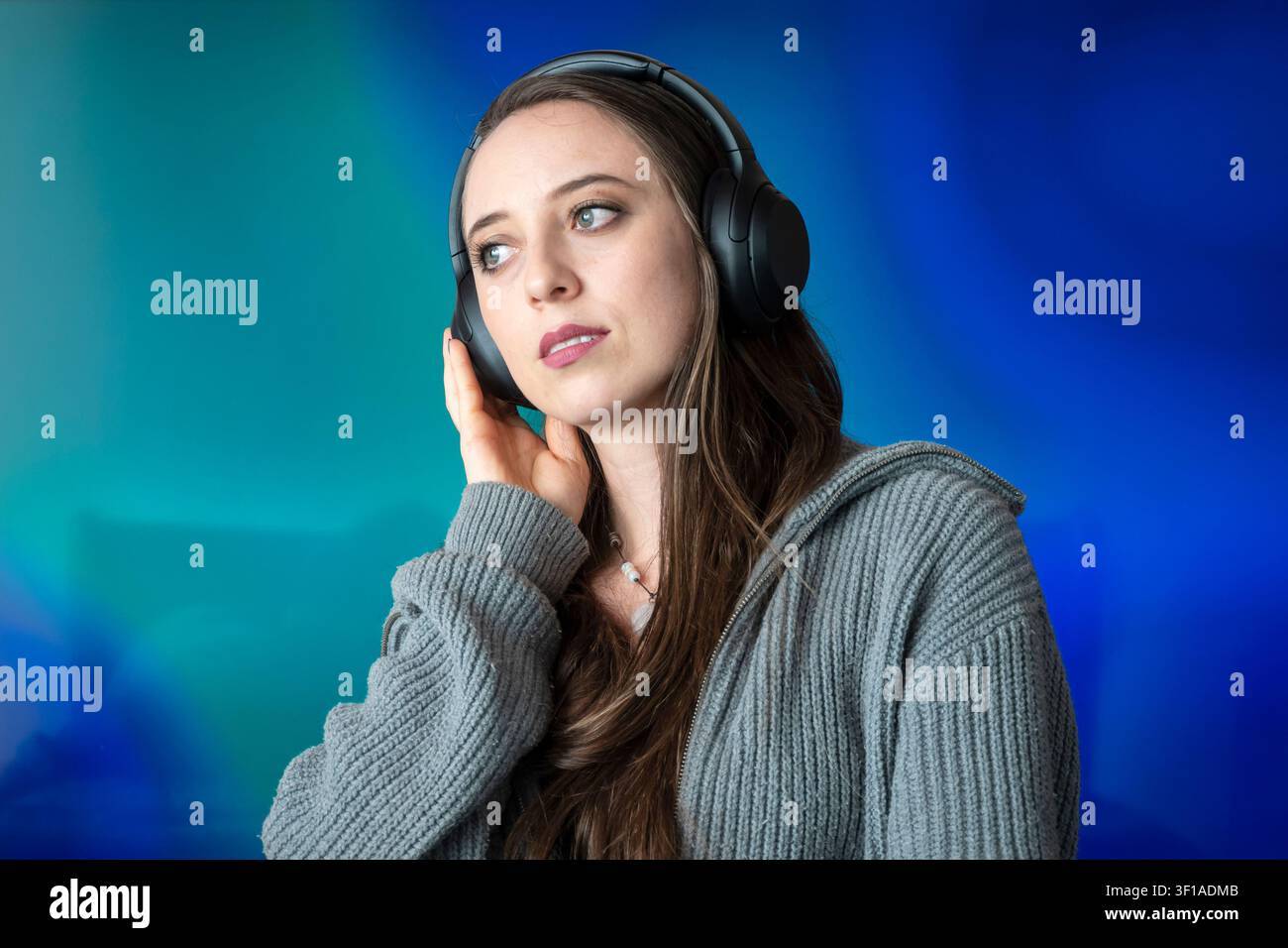 Junge Frau, verloren in Gedanken, hört Musik mit kabellosen Kopfhörern Stockfoto
