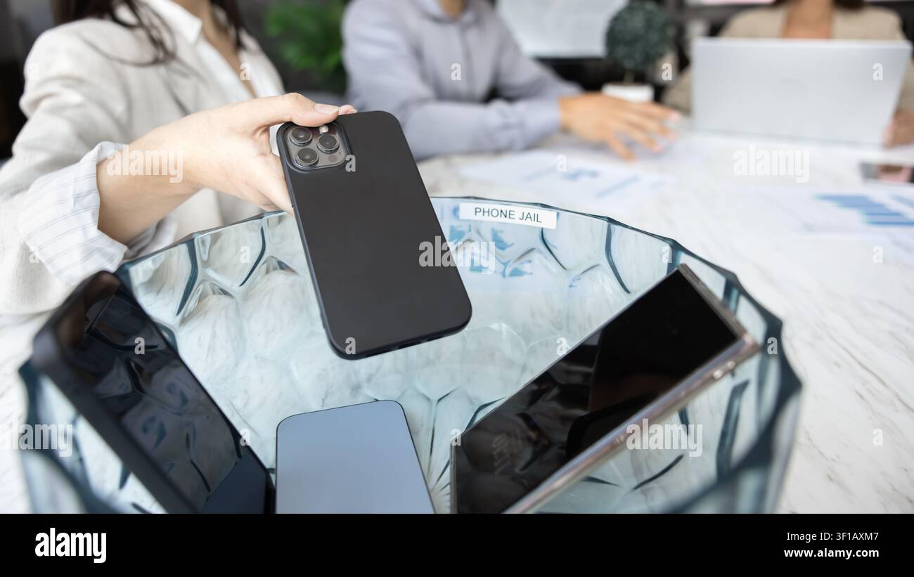 Teilnehmer eines Meetings, der sein Handy in den Bürotelefon-Gefängnis steckt, Nahaufnahme Stockfoto