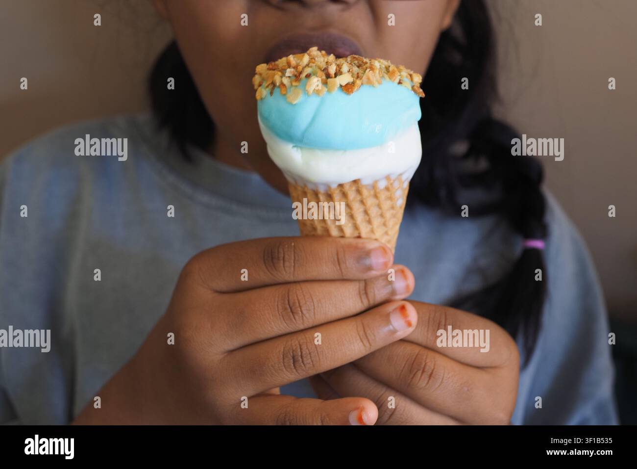 Ein Kind genießt eine Eisdose mit einer blauen Kugel und Nüssen oben drauf Stockfoto
