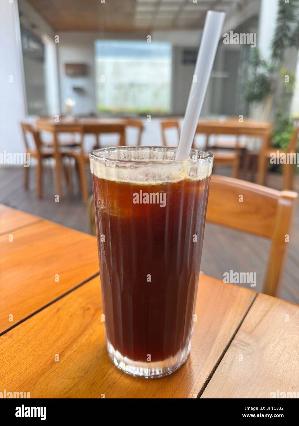 Erfrischender Eiskaffee Americano in einem klaren Glas mit Eiswürfeln auf einem Holztisch in einem modernen Café serviert, der einen gekühlten Spezialkaffee bietet Stockfoto