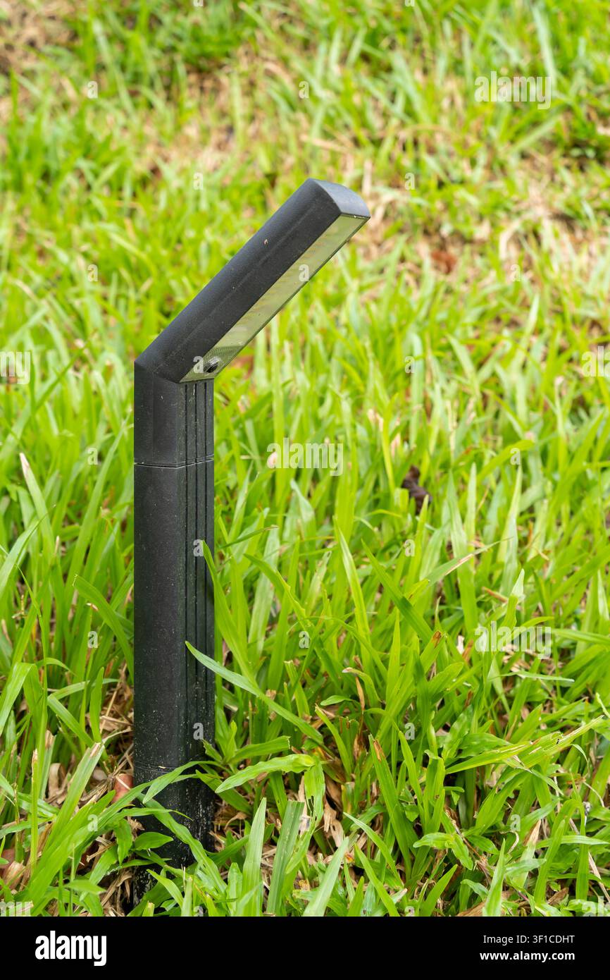 Eine moderne schwarze LED-Bodenleuchte steht zwischen üppigem grünem Gras und bietet stilvolle Wegbeleuchtung für Gärten, Parks und Außenlandschaften. Stockfoto