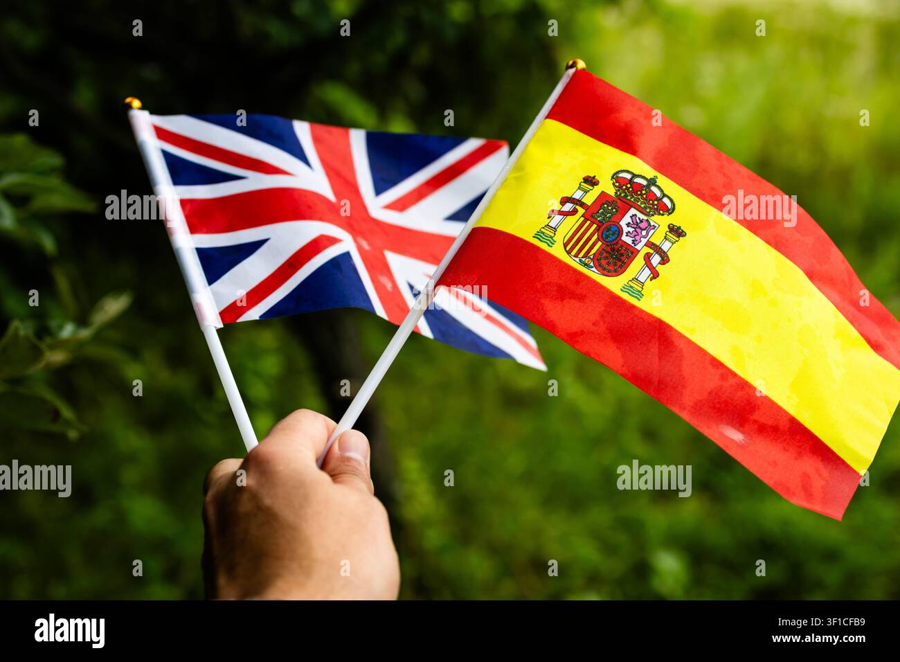 Miniatur-Britische und Spanische Flaggen wehen gemeinsam in einer Sommerlandschaft und drücken Einheitserbe und Gemeinschaftsgeist aus, während sie inspirierende Ferien verheißen Stockfoto