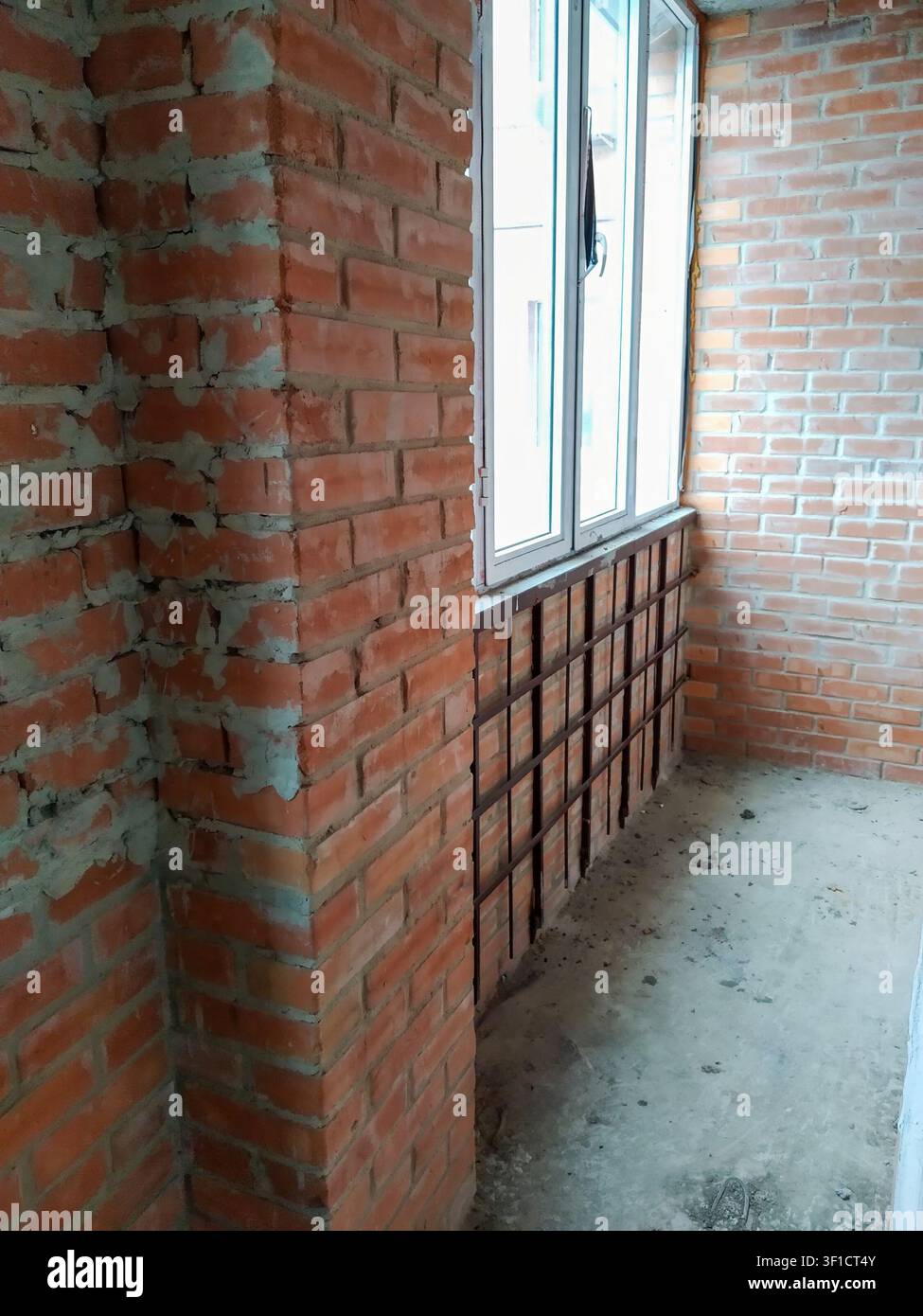 Ein roher, unlackierter Innenraum mit Ziegelmauern und einem großen Fenster, der auf Renovierung und den letzten Schliff wartet Stockfoto