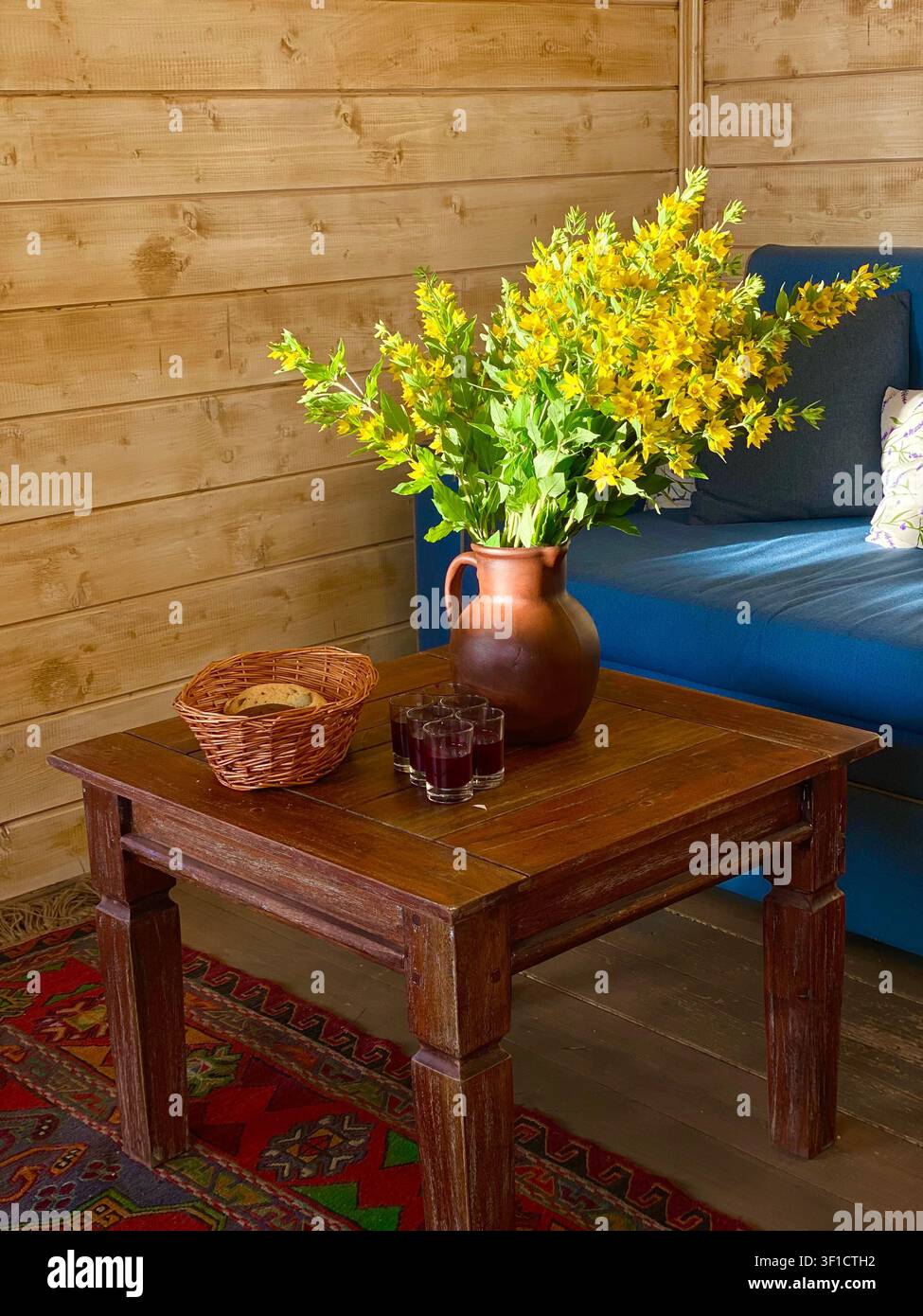 Rustischer Holztisch mit gelben Wildblumen in einer Keramikvase in einem gemütlichen Landhaus. Stockfoto