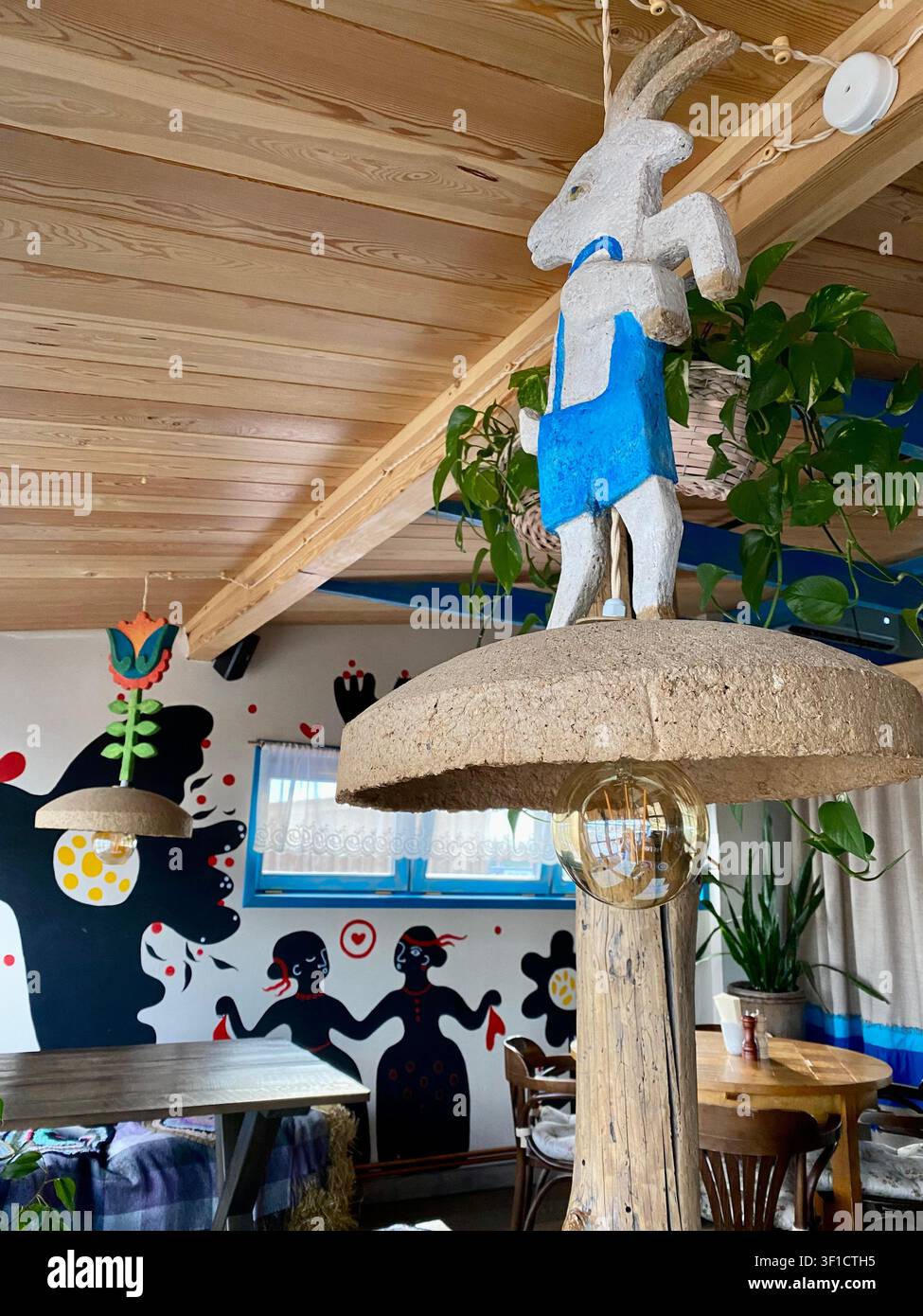 Rustikales Restaurantinterieur mit Volkskunst-Dekor, hölzerner Decke und handgefertigter Hängelampe bei Tageslicht. - Smartphone-aufgenommenes Stockfoto