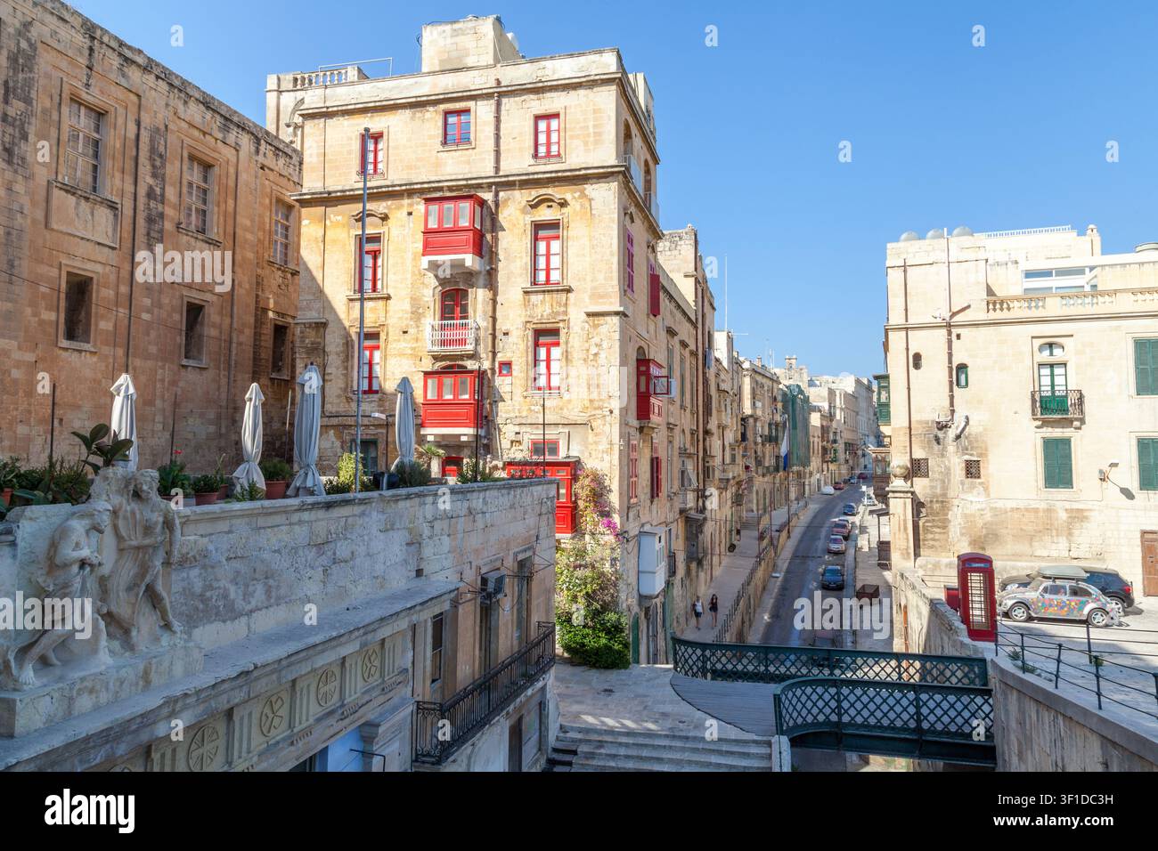 Ein traditionelles maltesisches Gebäude mit roten umschlossenen Balkonen steht an der Triq Il-Batterija Il-Belt, gesäumt von Kalksteinfassaden in Valletta, Malta Stockfoto