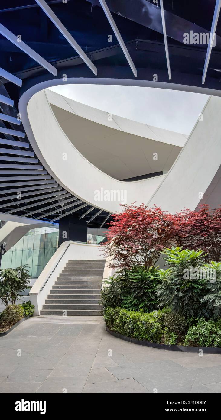 Ein atemberaubendes architektonisches Design zeigt sanfte Kurven und scharfe Winkel, umgeben von lebendiger Vegetation. Üppige Pflanzen und Bäume schaffen eine ruhige Atmosphäre Stockfoto