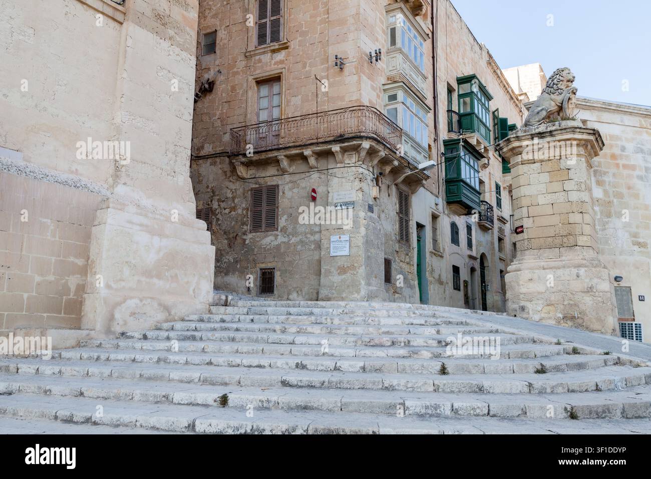 Breite Steinstufen führen zu einem Eckgebäude mit grün verschalten Balkonen und der De Vilhena Löwenstatue in der East Street, Valletta, Malta Stockfoto