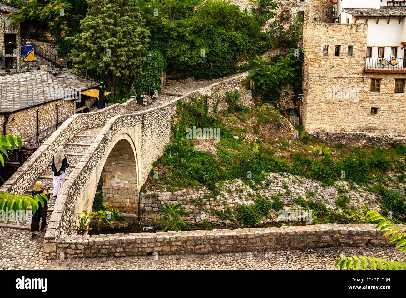 Historische krumme Brücke in Mostar über den Fluss mit alten Stadtgebäuden und Besuchern Stockfoto