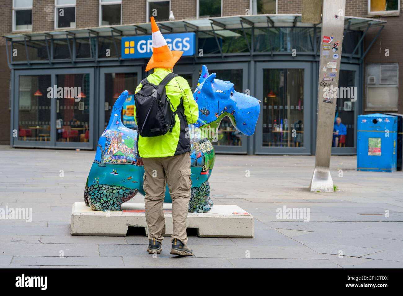 Ein Mann, der einen Verkehrszylinder trägt, betrachtet die Wanderlust Scotties Dog Skulptur, Buchanan Bus Station, Glasgow, Schottland, UK Stockfoto