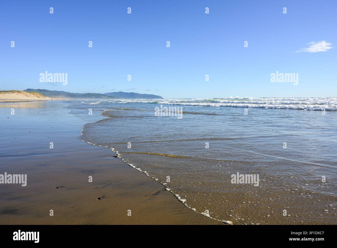 Hintergrund einer sanften Welle, die an einen Sandstrand rollt, mit blauem Himmel und Meereswellen Stockfoto