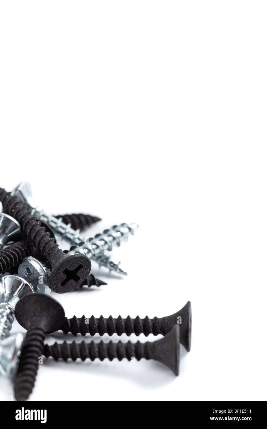 Schwarze und silberne Schrauben liegen verstreut auf Weiß. Einige haben scharfe Spitzen, andere flache Köpfe. Metallischer Glanz kontrastiert mit matt-schwarzer Oberfläche. Nahaufnahme Stockfoto