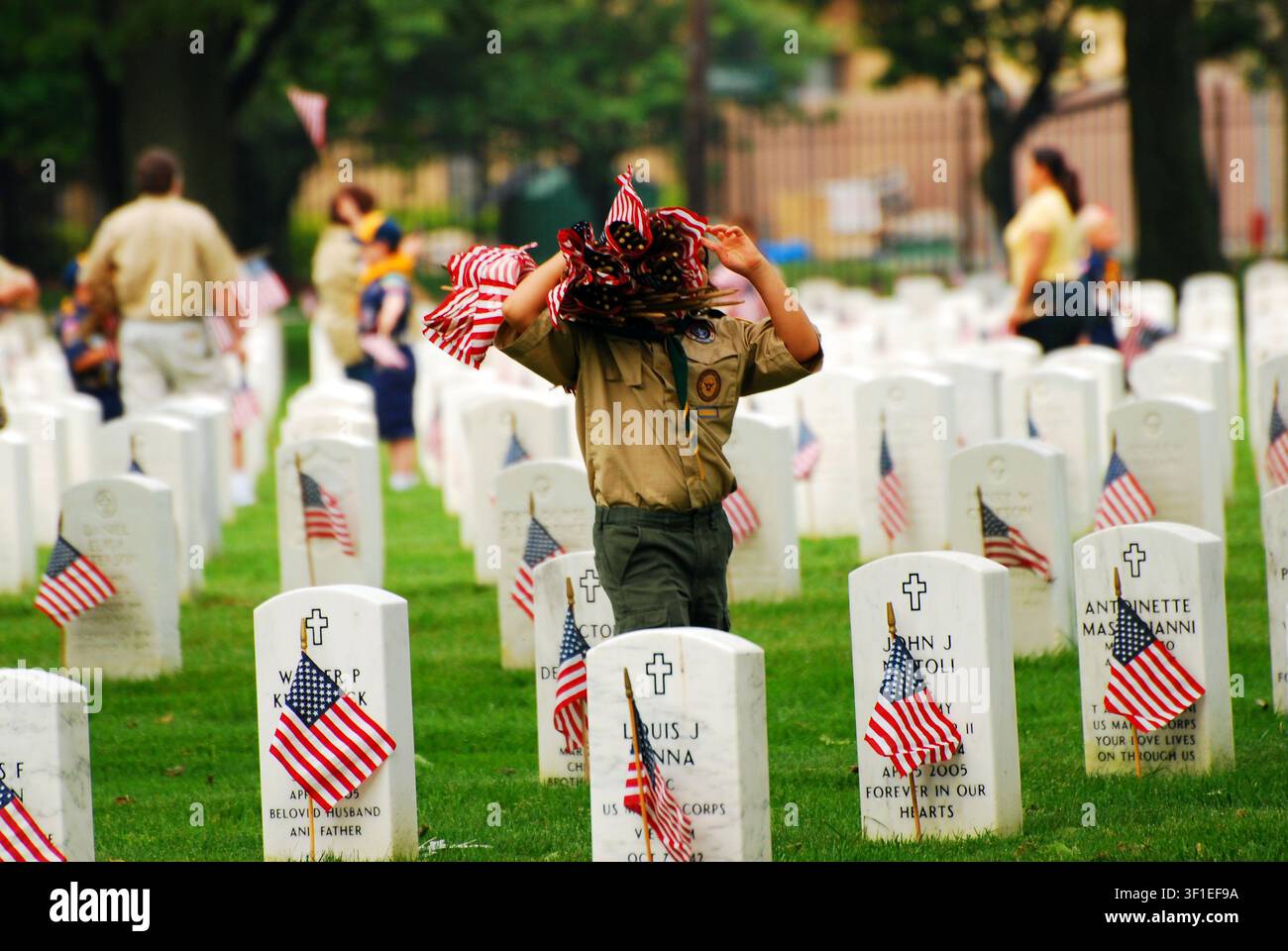 Ein Pfadfinder trägt einen großen Stapel amerikanischer Flaggen, um sie an den Gräbern von Soldaten und Dienstleistenden auf einem Militärfriedhof am Gedenktag zu platzieren Stockfoto