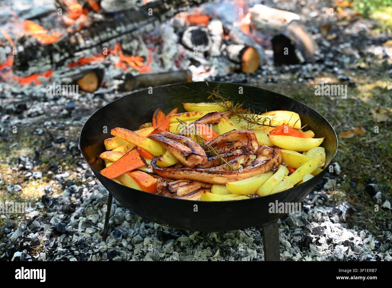 Kartoffeln und Tintenfisch gebacken auf dem Kamin in einer Bratschale mit Rosmarin, Karotte und Zwiebel Stockfoto