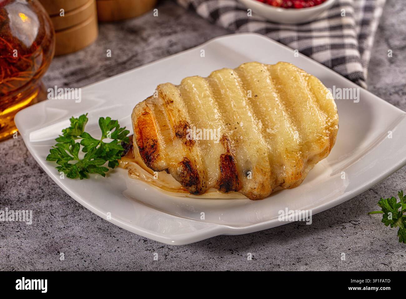 Goldener gegrillter Halloumi-Käse mit deutlichen Grillspuren, serviert auf einem weißen quadratischen Teller. Garniert mit frischer grüner Petersilie Stockfoto