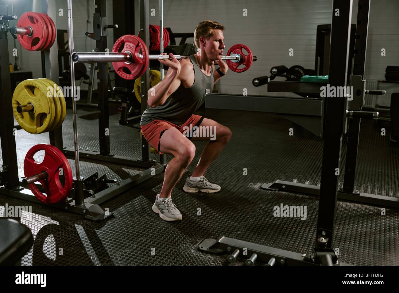 Männlicher Athlet trainiert mit Langhantelsquats im Fitnessstudio für Kraftzuwachs Stockfoto