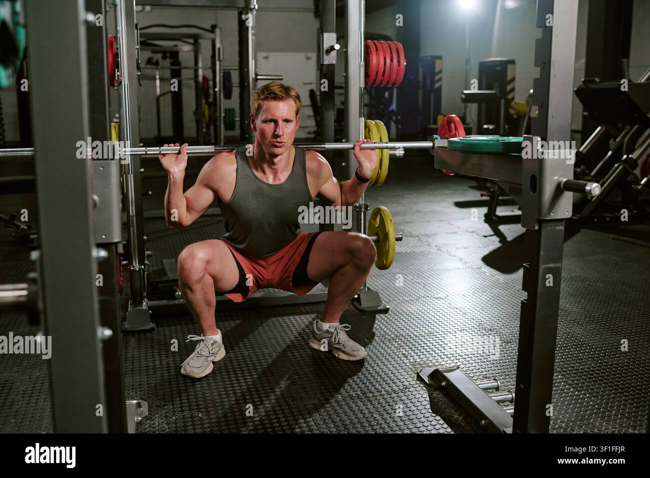 Junger Erwachsener führt beim Krafttraining einen Langhantelsquat durch Stockfoto