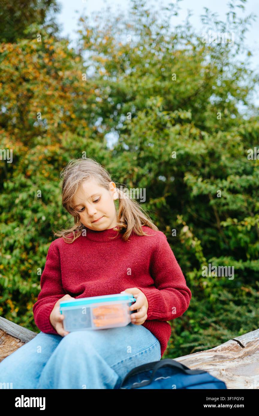 Schulmädchen hält eine gesunde Lunchbox, während es draußen sitzt Stockfoto