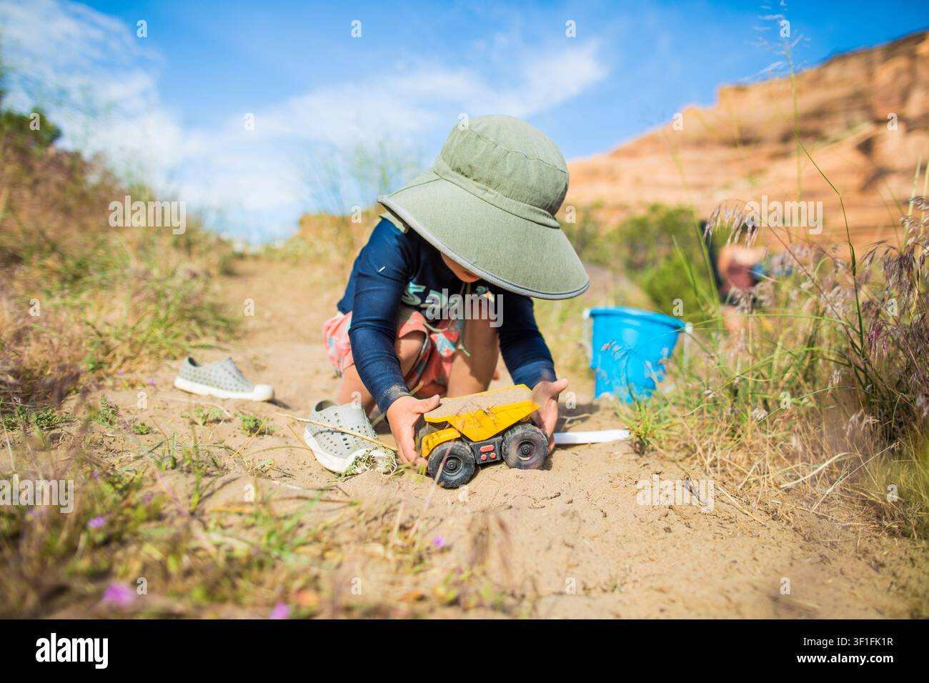 Kleiner Junge spielt mit einem Spielzeugkipplaster im Sand Stockfoto