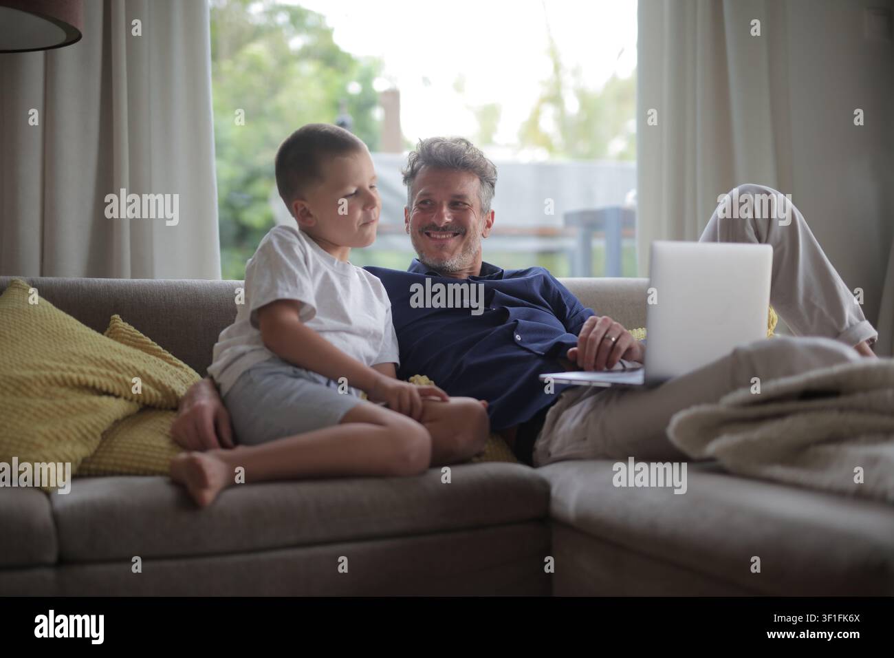 Zufriedener Vater und Sohn, die zu Hause auf der Couch sprechen Stockfoto