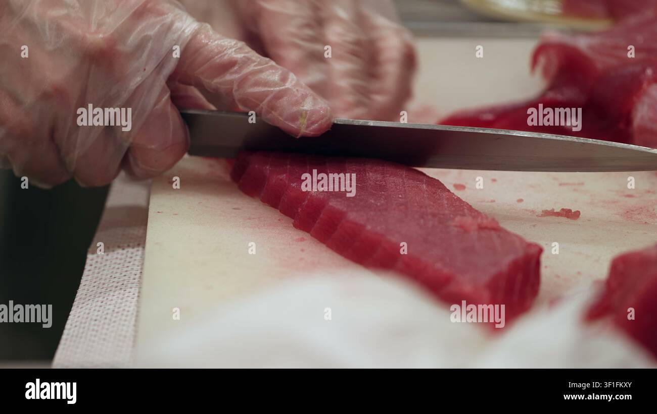 Professioneller Koch schneidet frisches rohes Thunfischsteak auf einem weißen Schneidebrett Stockfoto